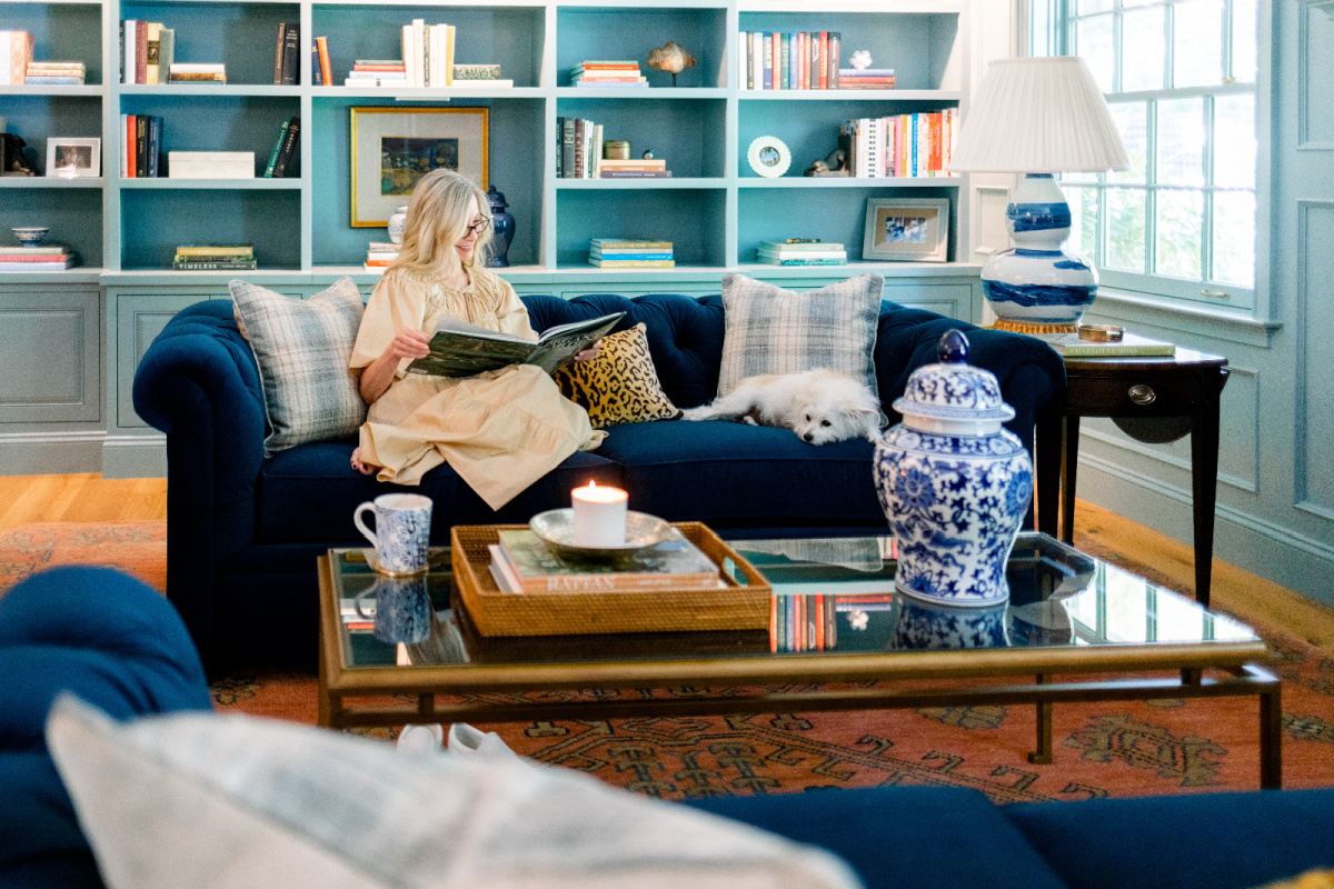 Woman reading book on blue velvet sofa with dog