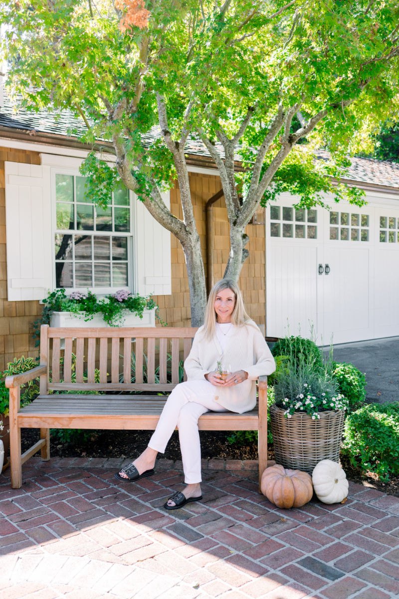 Woman sitting on teak bench decorated for fall