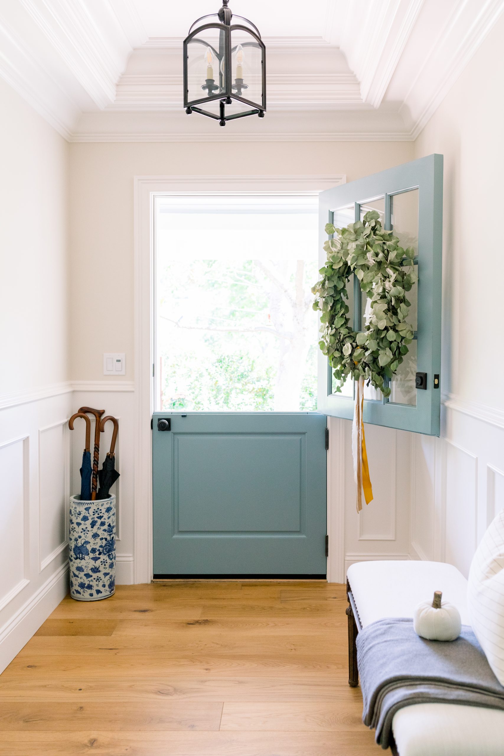 Foyer looking through open blue Dutch door with wreath, bench and pumpkins