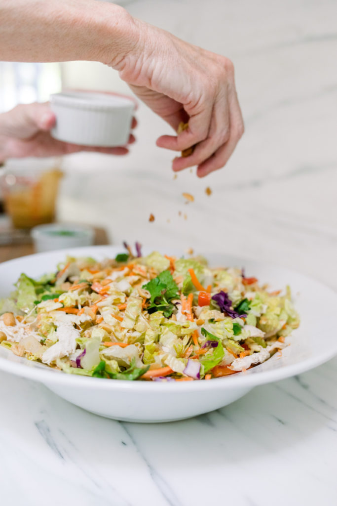 Adding peanuts to Asian chicken salad bowl