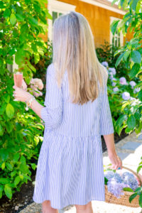Woman holding cocktail and flower basket in garden Rose Hibiscus Spritz