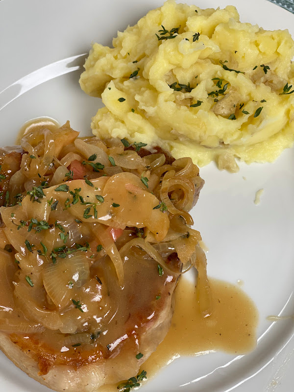 Plated pork chop with onion apple cider gravy and mashed potatoes.