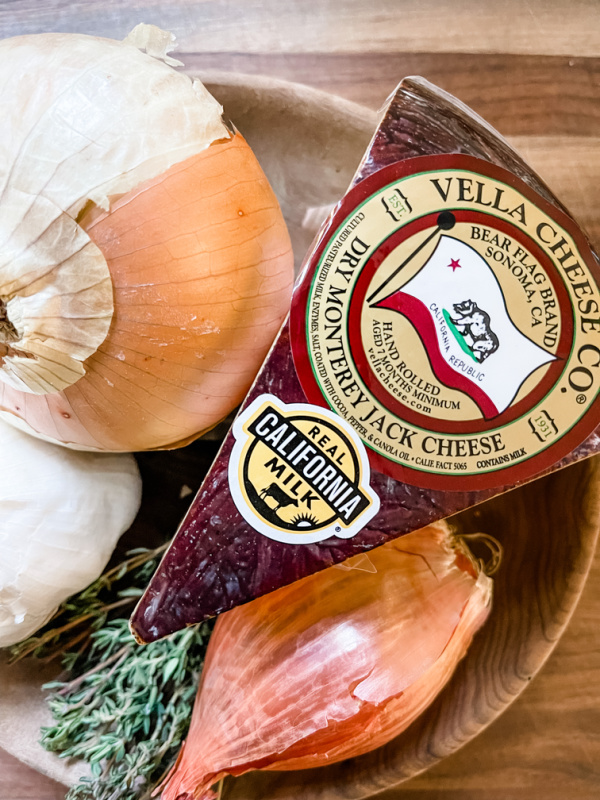 Wedge of Vella dry jack in a wooden bowl of onions and herbs.