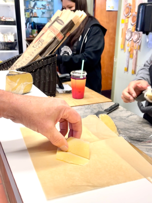 Man picking up cheese sample at cheese store.
