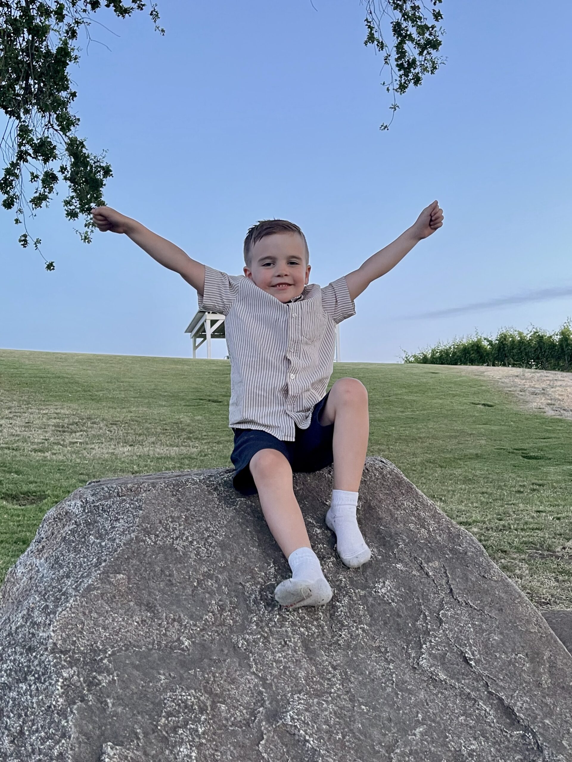 Little boy sitting on rock with hands in air.