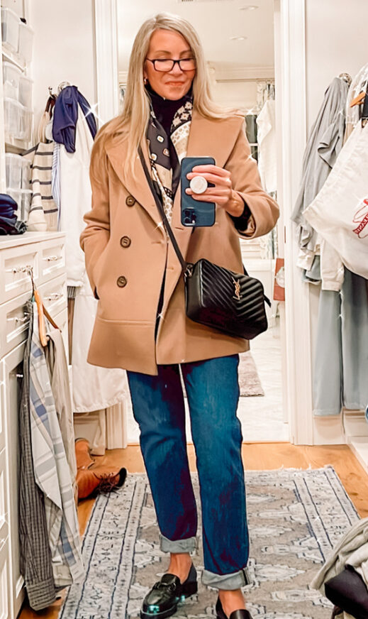 Woman taking mirror selfie wearing camel coat.
