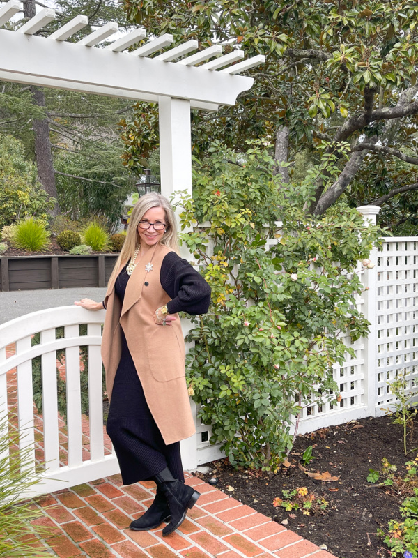 Woman wearing black dress and camel coat vest.
