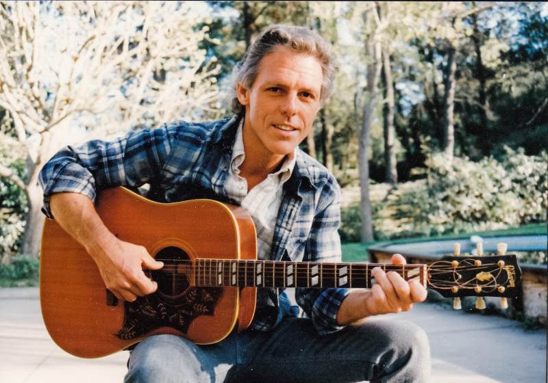Man playing guitar in backyard.