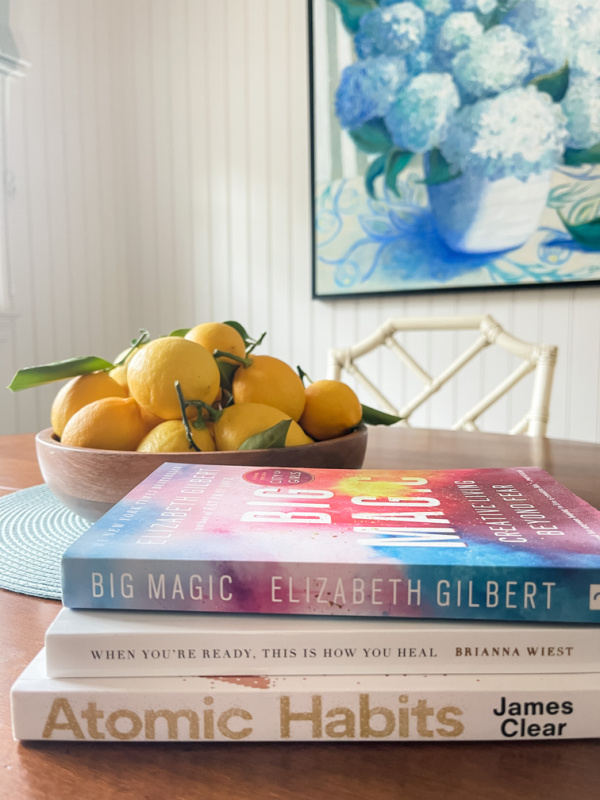 Bowl of lemons next to stack of books on table.