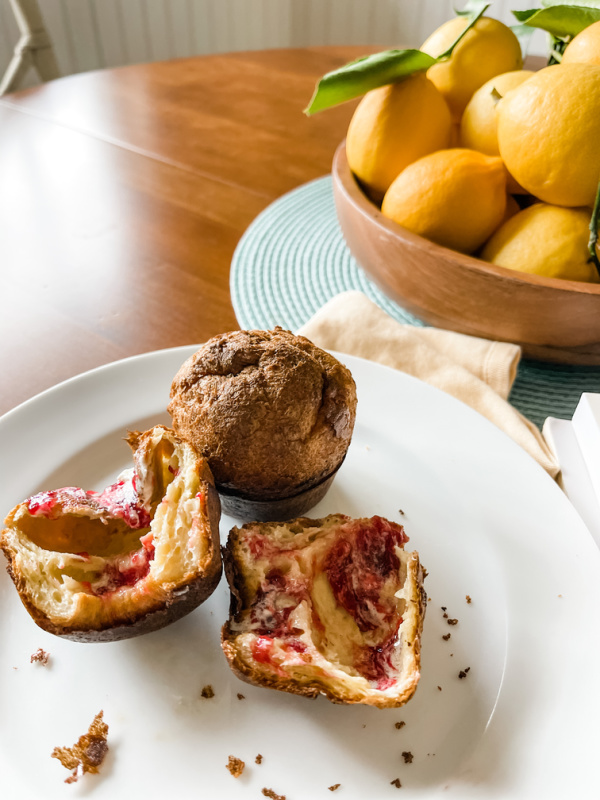 Popovers on plate with butter and jam and bowl of lemon in background.