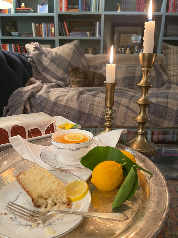 Silver tray with teacup and slice of cake, candles burning and cat on sofa.