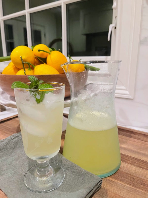 Fresh lemonade in pitcher and iced glass with bowl of lemons in background.