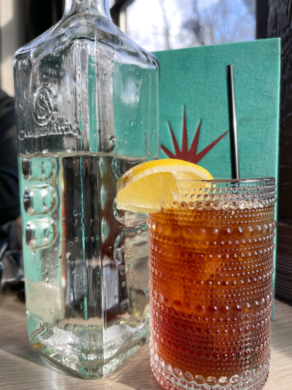 Ice Tea glass next to water bottle and bar menu on table.