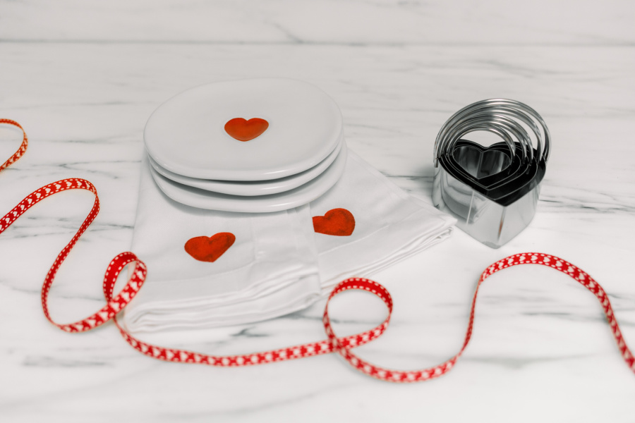 Valentine dessert plates and napkins next to heart ribbon and cookie cutters.