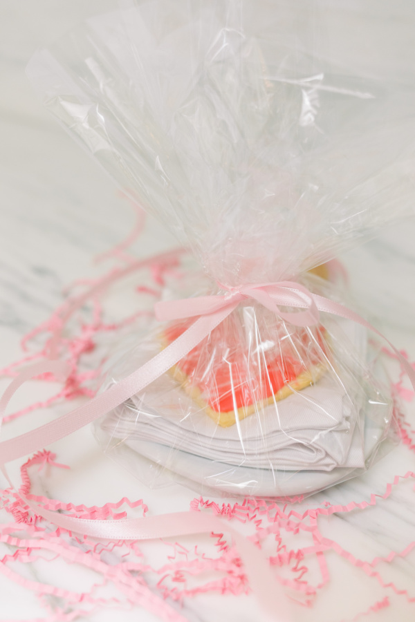 Heart shaped cookie on plate wrapped with cellophane and surrounded with pink confetti.