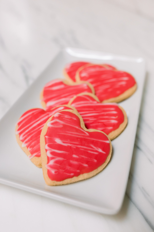 Pink frosted heart shaped cookies on white tray.
