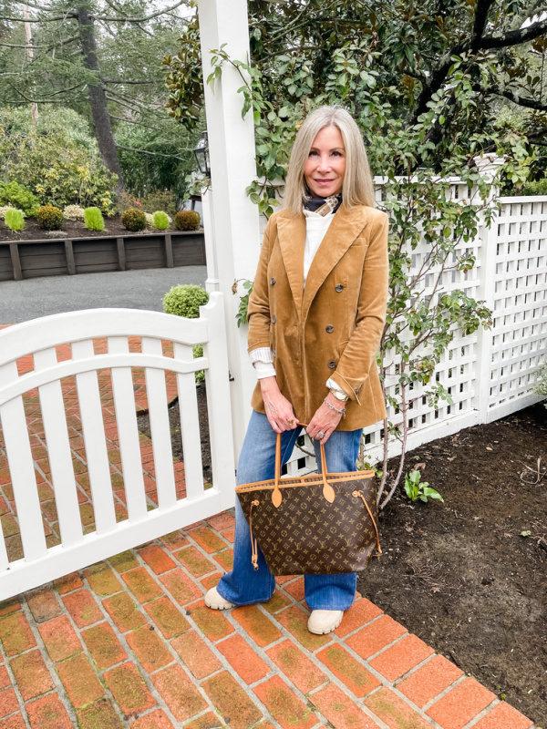 Woman wearing corduroy blazer and denim standing in front of white fence.