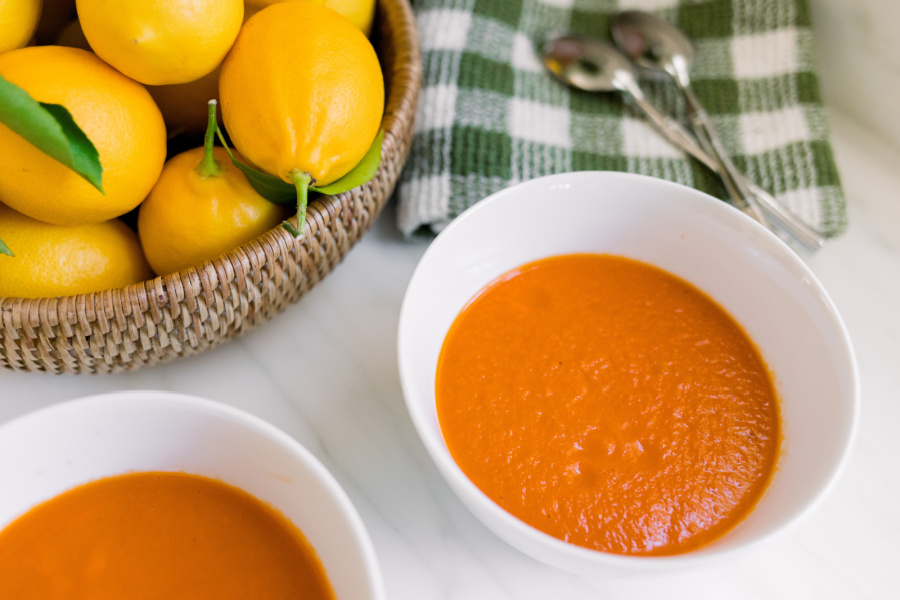 Bowls of tomato soup next to a bowl of lemons and green and white dishcloth.