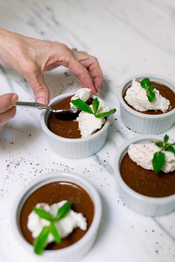 Ramekins filled with chocolate pots de creme with whip creme and mint sprigs on top.