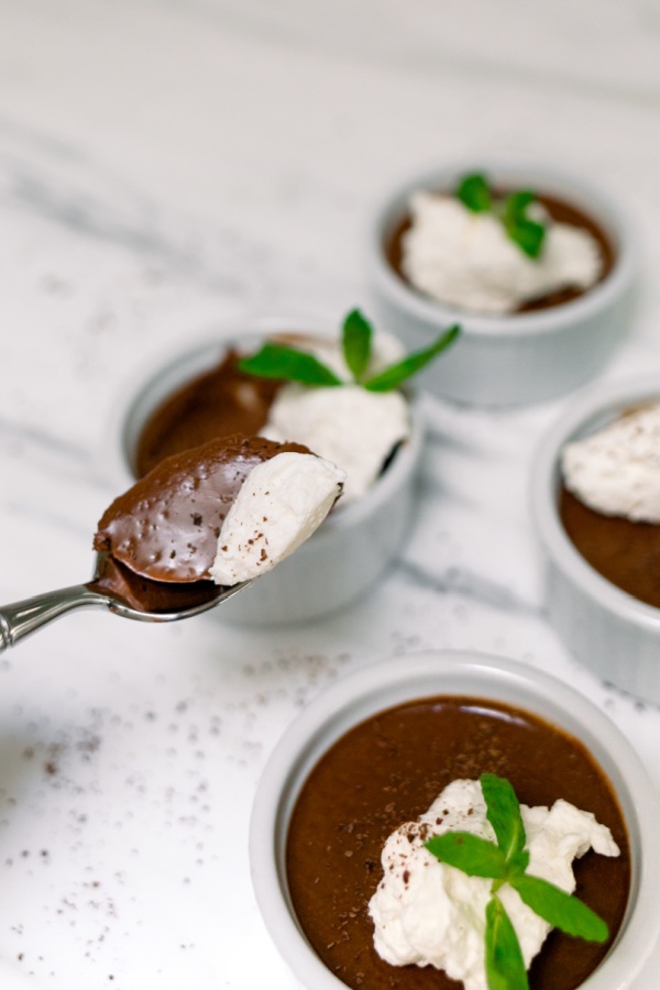 Ramekins filled with chocolate pots de creme with whip creme and mint sprigs on top.