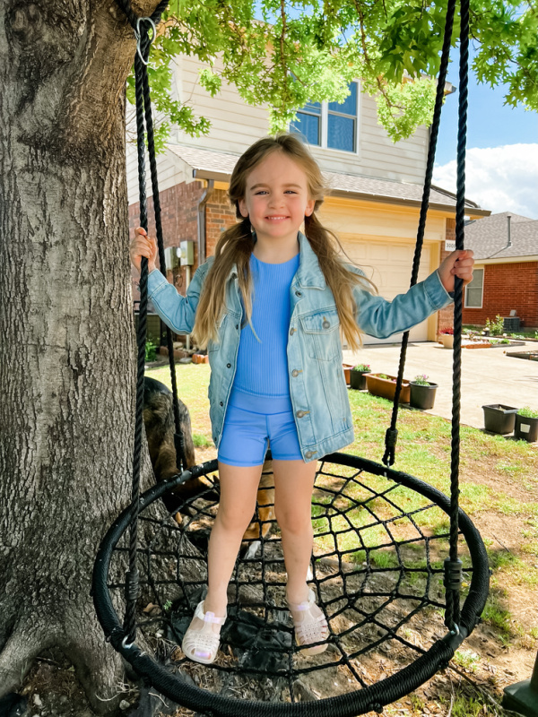 Little girl in denim jacket on swing.