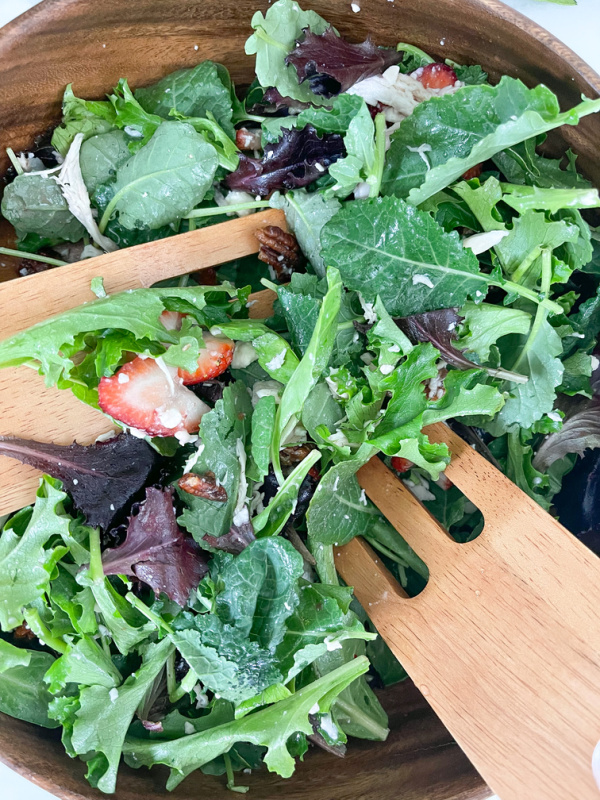 Spring salad in wooden salad bowl with tongs.