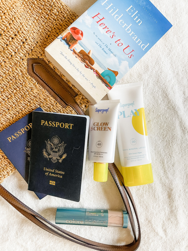 Passports, sunscreen and beach read on straw tote.