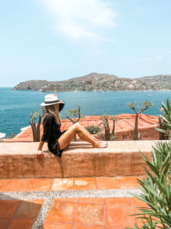 Woman wearing black coverup and hat overlooking ocean in Zihautanejo.