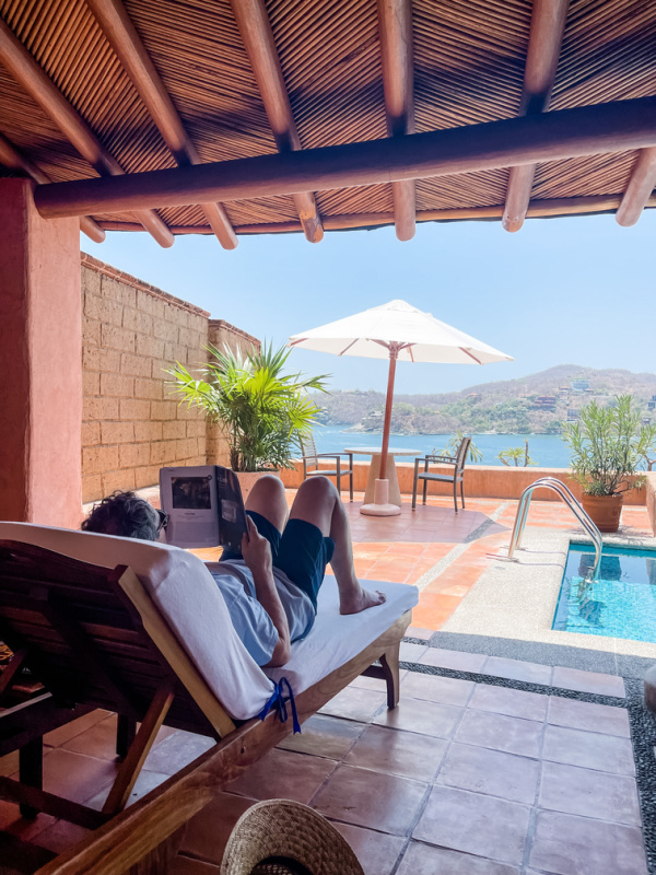 Man laying on chaise lounge poolside reading.