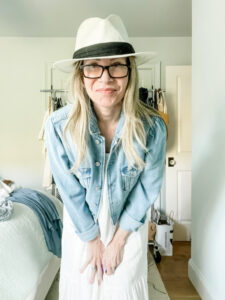 Woman wearing white dress, denim jacket and Panama hat.