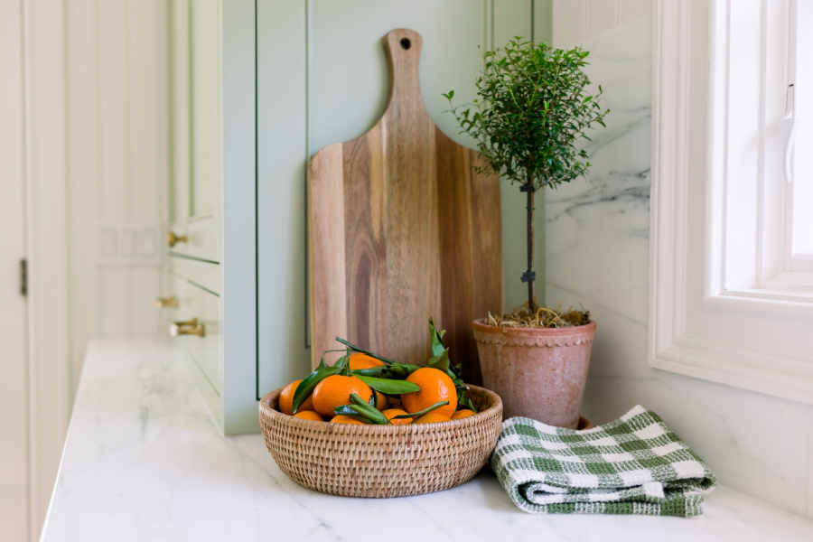 Kitchen vignette with cutting board leaning against counter, topiary and bowl of oranges.
