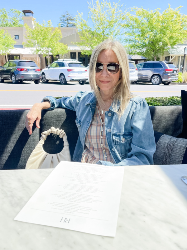 Woman sitting at outdoor table with menu in front of her.