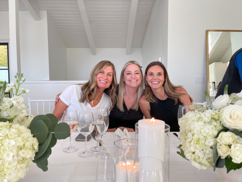 Three women at dinner table with candles and white flowers.