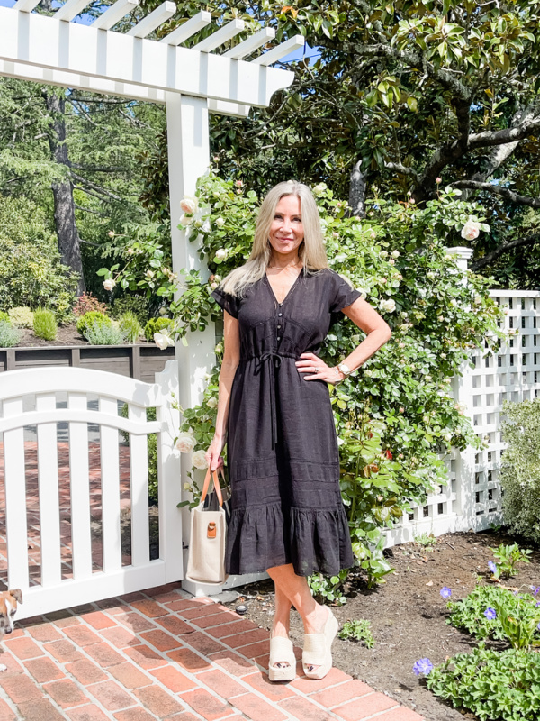 Woman wearing black Rails Kiki dress standing in front of garden gate.