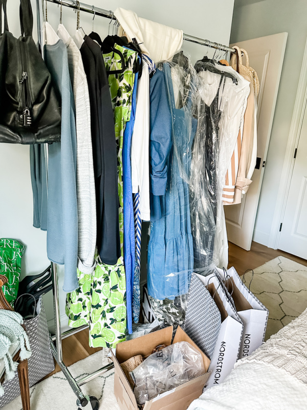 Messy rolling rack full of clothes to pack for trip.