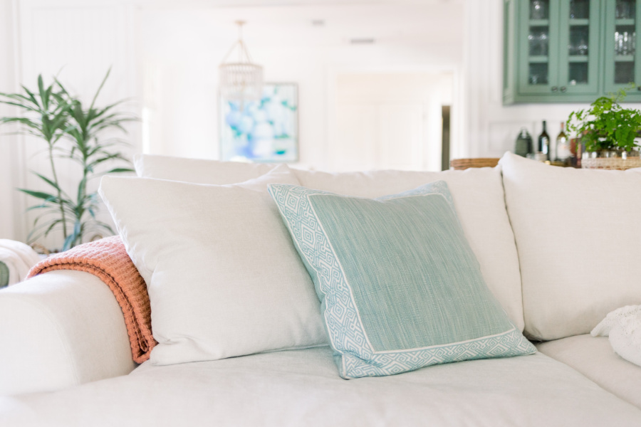 White sofa with blue pillows and coral throw blanket.