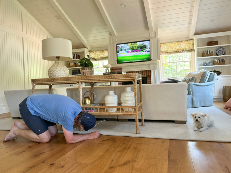 Man on hands and knees looking underneath family room table.