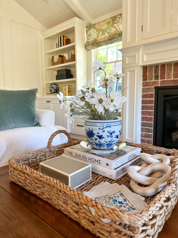 Woven tray filled with flowers and other things on a coffee table.