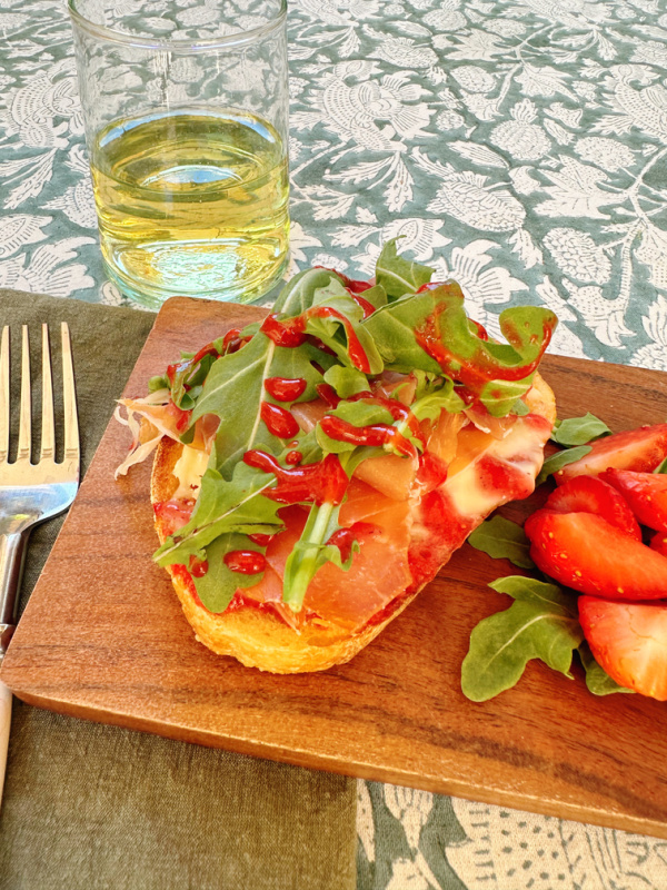 Tartine and salad on bread board next to small glass of wine.