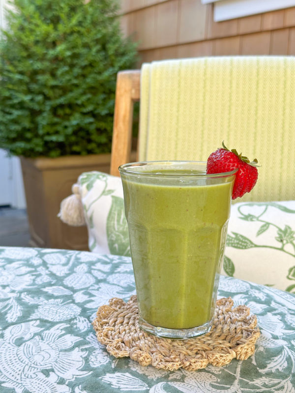 Kale and strawberry smoothy sitting on outdoor dining table.