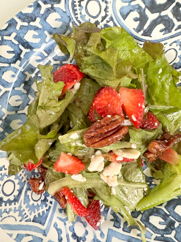 Salad on blue and white plate with strawberries and candied pecans.