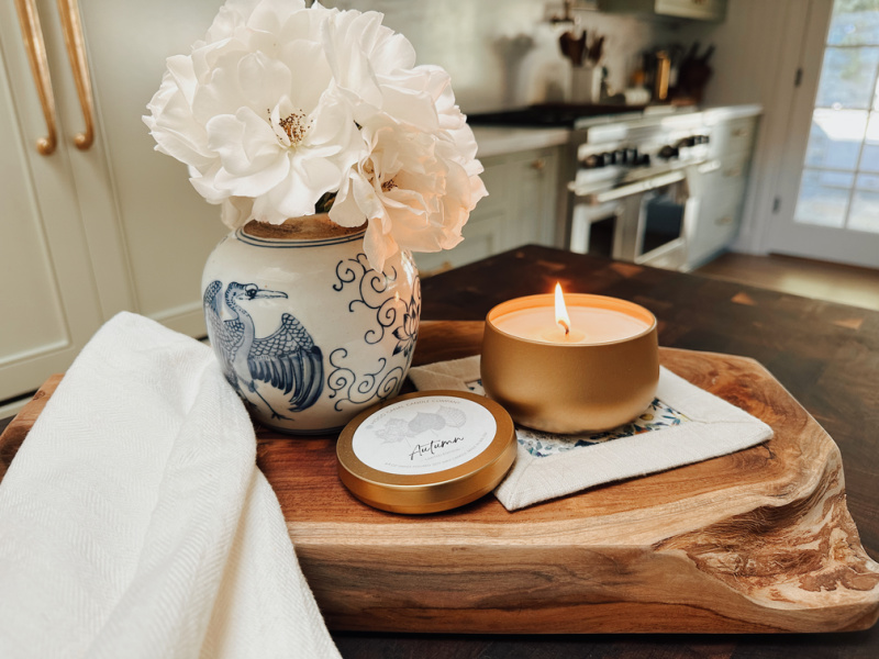 Autumn candle next to blue and white vase of roses on kitchen island.