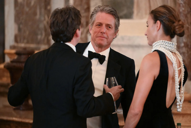 Hugh Grant and his wife talking to another man at Versatile state dinner.