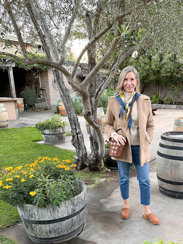 Woman wearing camel coat standing outside Swiss Hotel in Sonoma on fall evening.