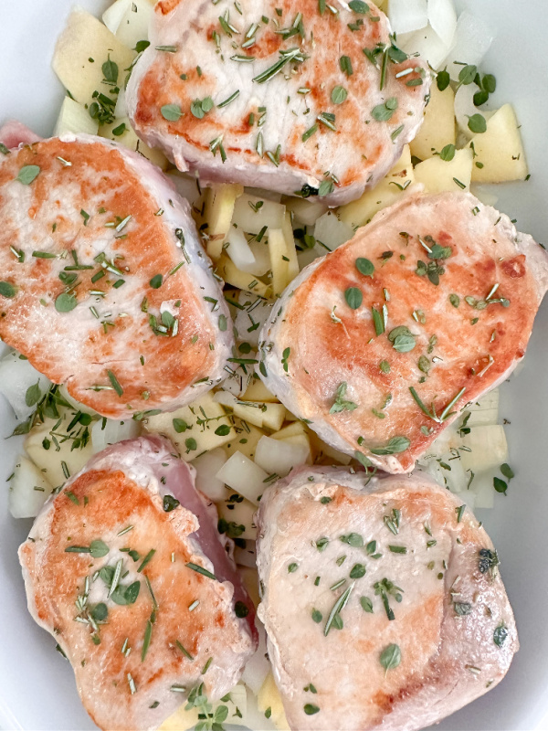 Browned pork chops over apples and onions in baking pan.