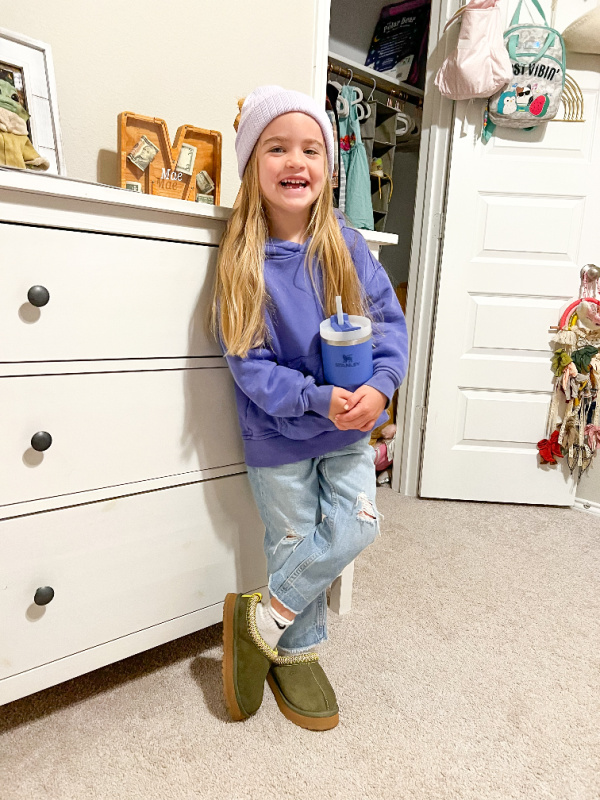 Little girl leaning against a chest of drawers wearing Ugg slippers.
