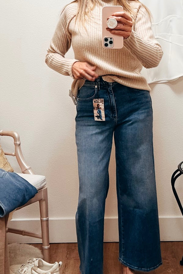 Woman taking dressing room selfie wearing denim and cashmere sweater.