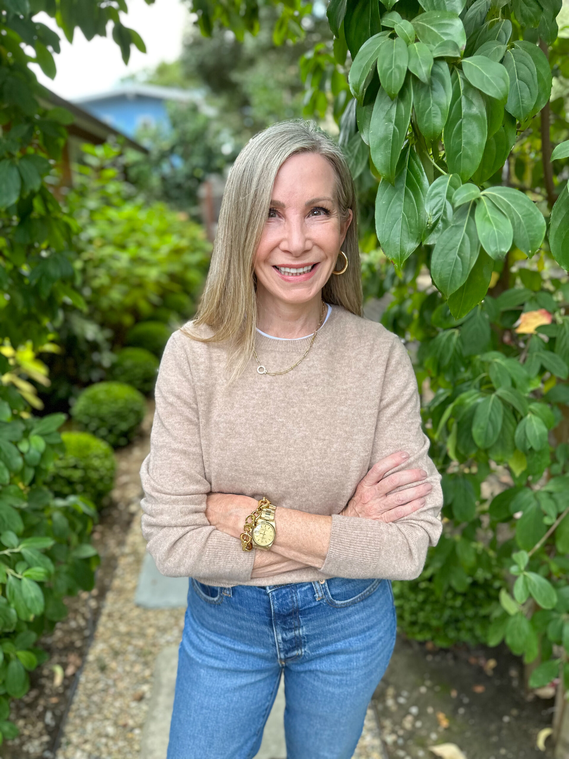 Woman wearing Quince cashmere sweater and jeans, standing in a garden.
