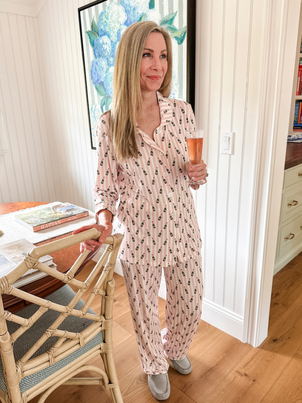 Woman holding sparkling rose glass wearing champagne bottle print pajamas.