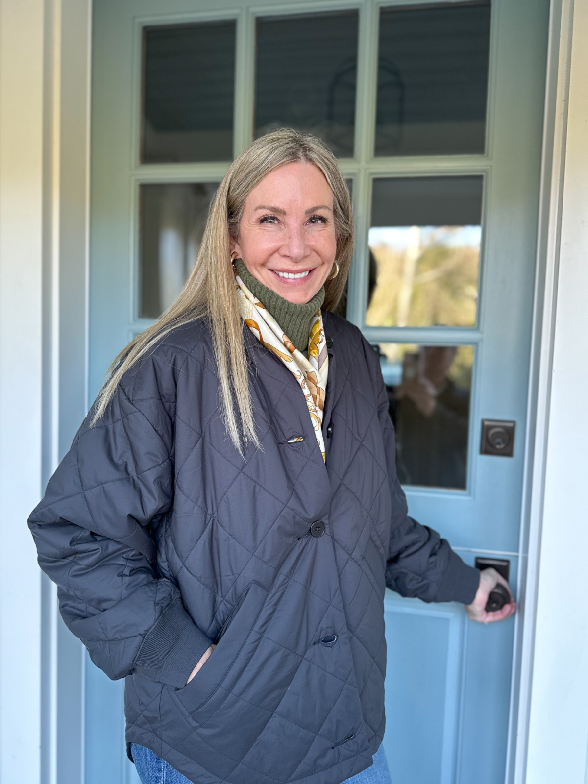 Woman wearing quilted jacked standing in front of blue Dutch door.